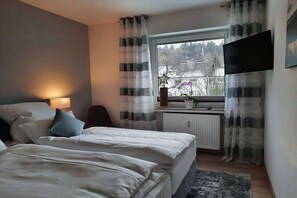 A hotel room with a bed, bedside table, lamp, window with curtains, radiator, and a flat-screen TV mounted on the wall. - Holiday apartment with 1 bedroom (Hahnenklee)