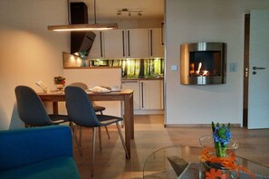 A modern living room with a dining area, a fireplace, and a kitchen in the background. - Holiday apartment with 1 bedroom (Hahnenklee)