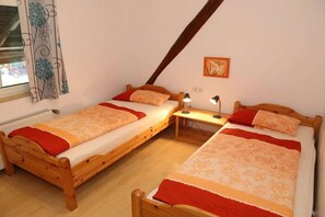 Ein Zimmer mit zwei Holzbetten, jedes mit einer roten Decke und einem Nachttisch mit einer Lampe.