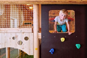 Ein Kind klettert auf eine hölzerne Spielkonstruktion mit Klettergriffen.