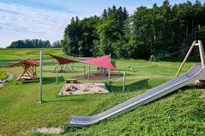 Ein Spielplatz mit Rutsche, Schaukeln und einem schattigen Bereich.