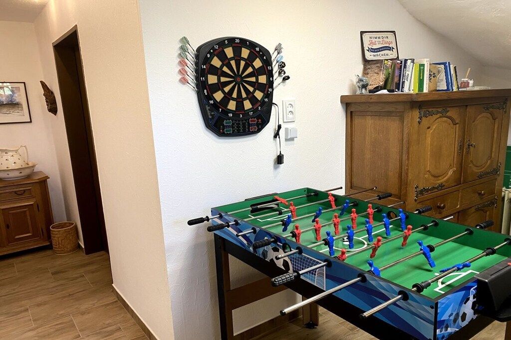 A room with a dartboard, a foosball table, and a wooden cabinet.