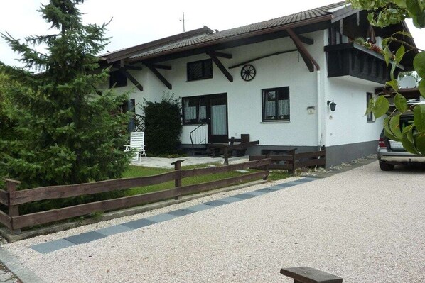 A white building with a wooden fence, a bench, and a car parked in front. - Monika House in Übersee am Chiemsee (Übersee)