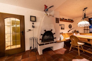 A room with a fireplace, a wooden door, a dining table with chairs, and a hanging lamp. - Monika House in Übersee am Chiemsee (Übersee)