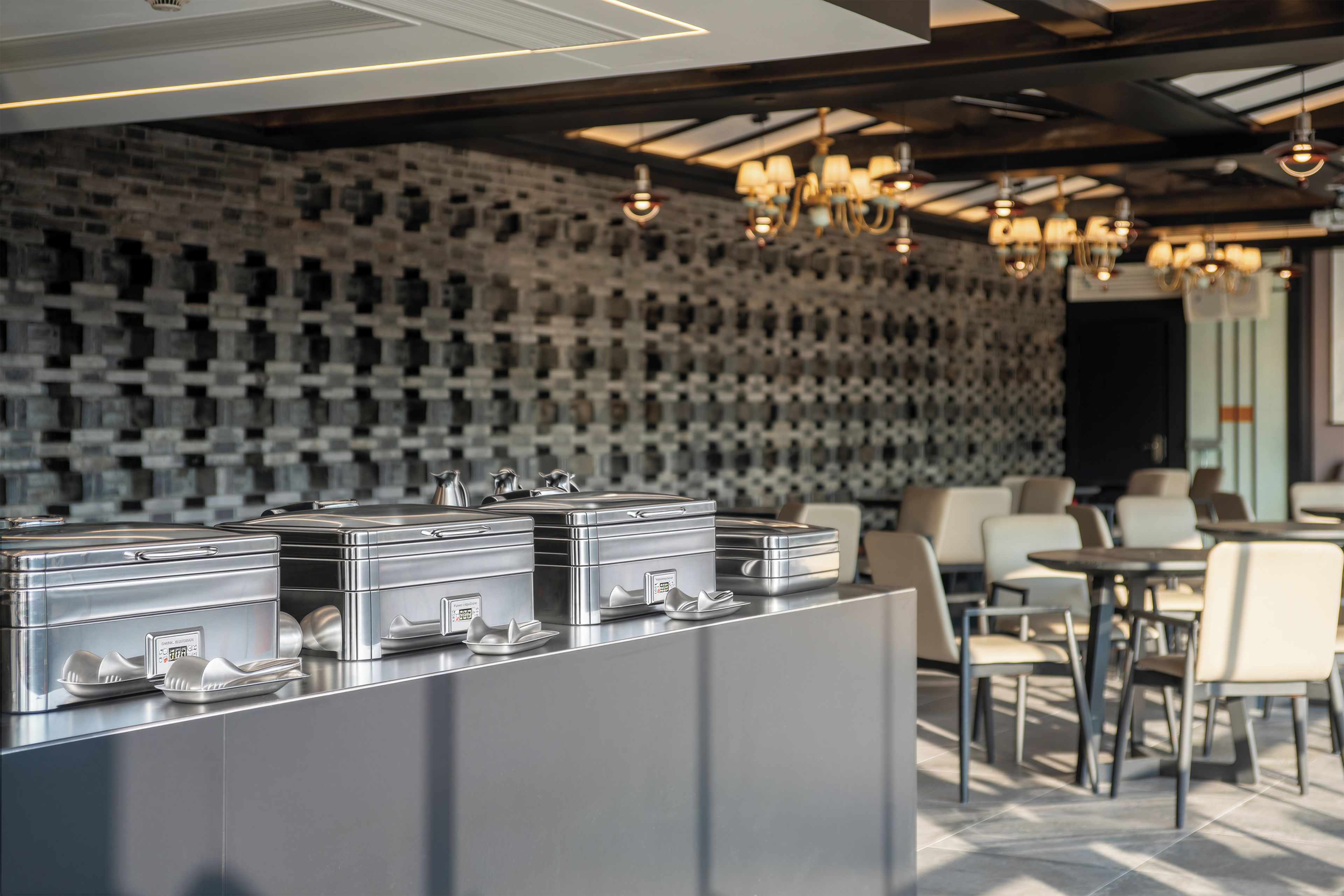 A modern interior with a wall of uniform square patterns, a reception area with metal storage units, and a seating area with tables and chairs.