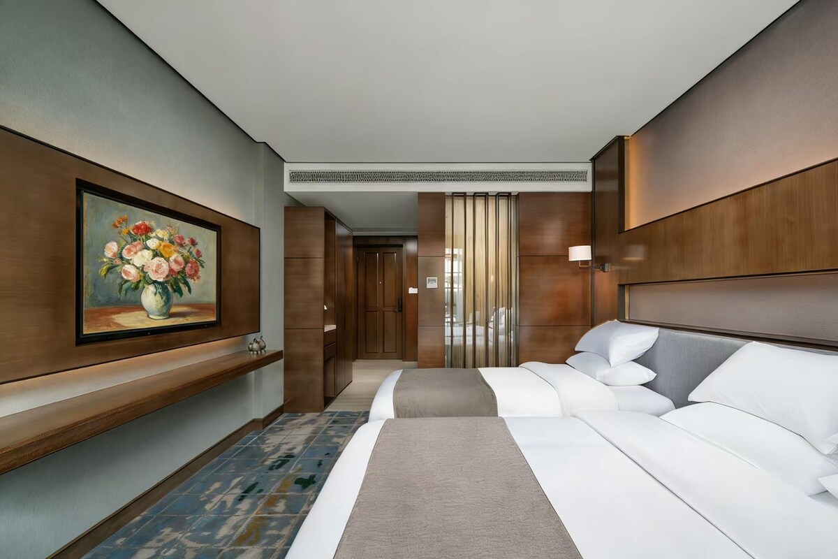 A hotel room with a bed, a painting, a nightstand, and a view of the hallway.