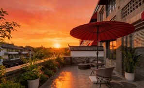 Um pátio com área de estar ao ar livre, um guarda-sol vermelho e vista para o pôr do sol.