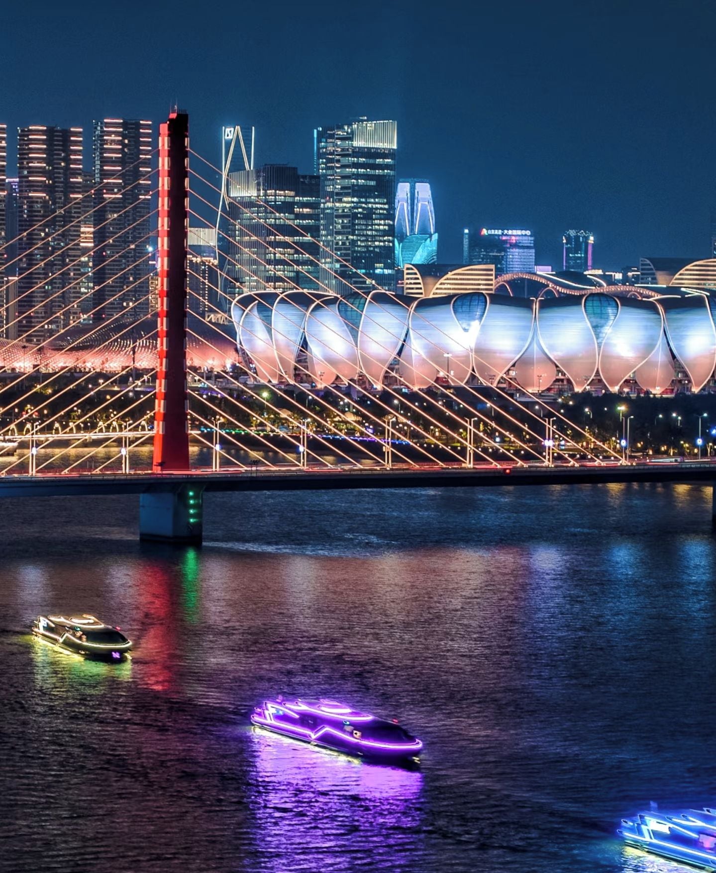 A nighttime cityscape with a prominent bridge and modern buildings.