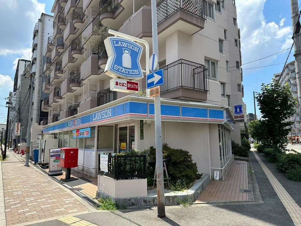A Lawson station with a blue and white facade, located on a city street with buildings in the background.