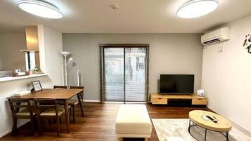 A modern living room with a wooden dining table, a white sofa, a TV, and a small round table.