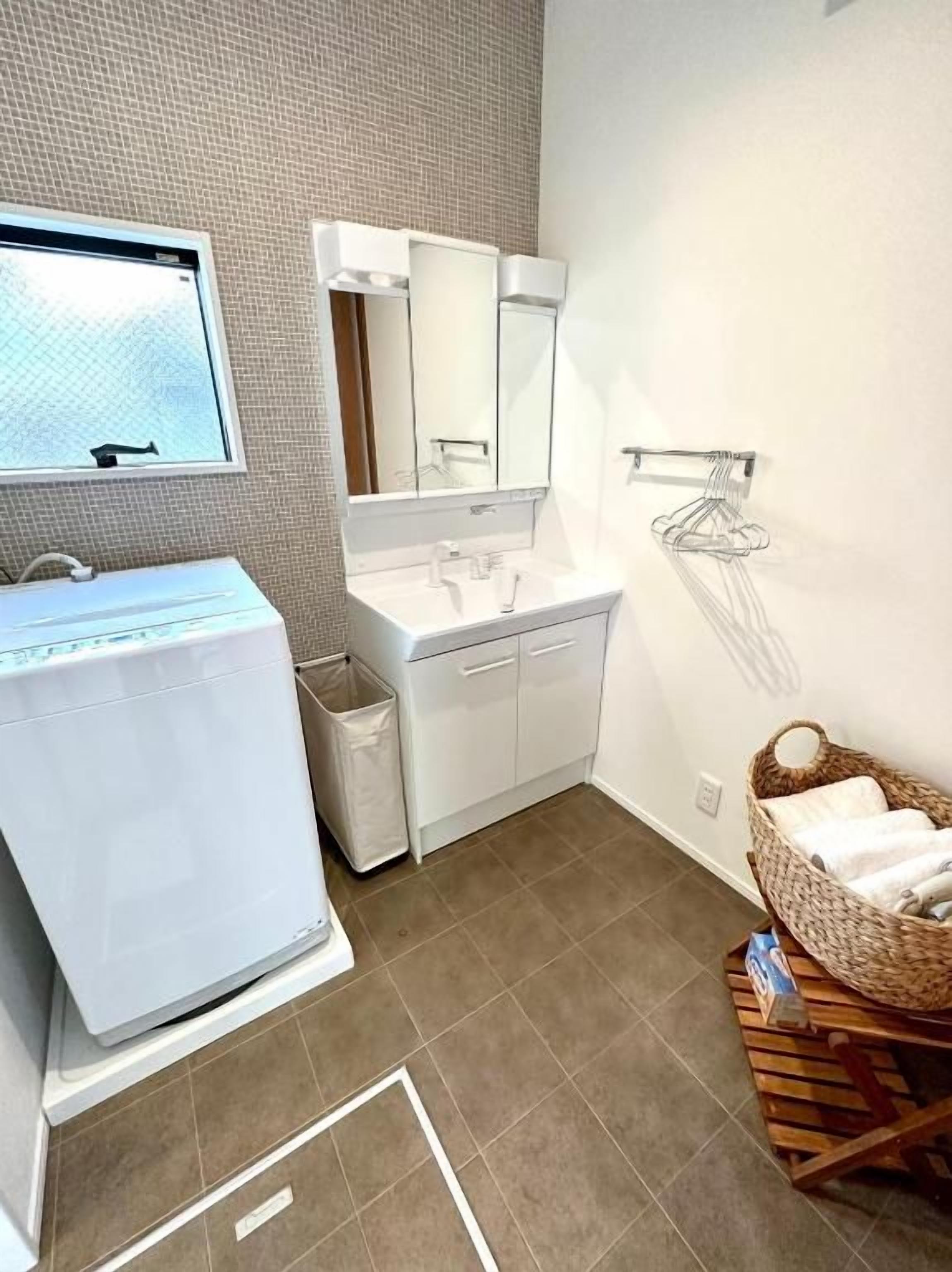 A modern bathroom with a washing machine, a sink, a mirror, and a towel rack.