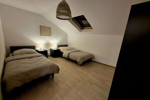 A bedroom with two beds, a nightstand with a lamp, a hanging light fixture, and a slanted ceiling. - Holiday home Schilz II (Plütscheid)