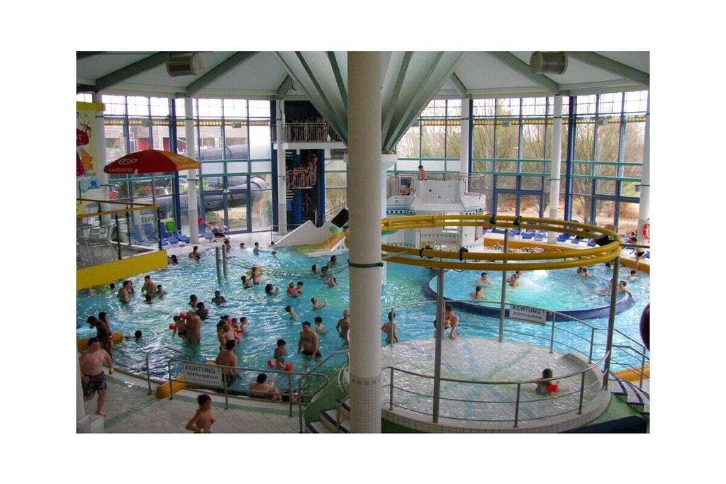 Une piscine intérieure dotée de plusieurs couloirs, d’un toboggan central et d’une plateforme d’observation.