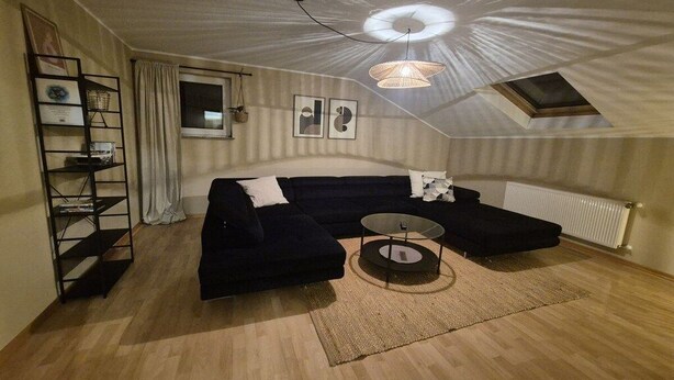 A modern loft bedroom with a sectional sofa, a round coffee table, and a skylight. - Holiday home Schilz II (Plütscheid)