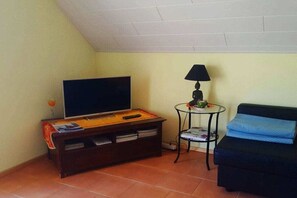 A living room with a television on a wooden stand, a small round table with a lamp, and a sofa with blue cushions. - Holiday apartment with 2 bedrooms (Wieden)