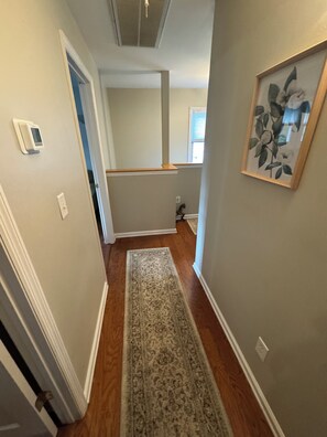 Un pasillo con piso de madera, un tapete, una puerta y un cuadro en la pared.