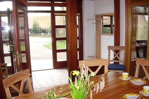 A room with a wooden dining table set for two, a blue cushioned chair, and a view of a green landscape through a glass door. - Holiday apartment with 2 bedrooms (Wölpinghausen)