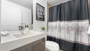 Casa de banho moderna com lavatório branco, sanita e cortina de chuveiro com padrão de árvore.