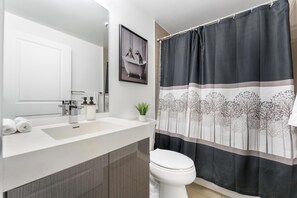 Ein modernes Badezimmer mit einem weißen Waschbecken, einer Toilette und einer Duschkabine mit Baummuster.