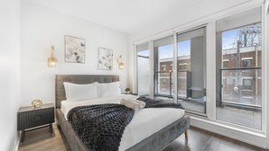 Quarto moderno com uma cama grande, mesa de cabeceira, janela com vista para a cidade e arte nas paredes.