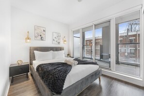 Ein modernes Schlafzimmer mit einem großen Bett, einem Nachttisch, einem Fenster mit Stadtblick und Wandbildern.