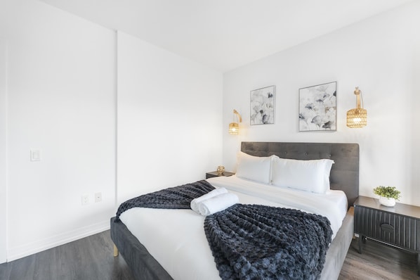 A modern hotel room with a large bed, two bedside tables, a nightstand, and wall-mounted sconces.