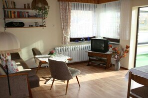 A living room with a sofa, a dining table, a TV, and a radiator. - Holiday apartment with 1 bedroom (Brottreode\/Trusetal)