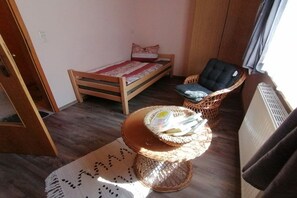 A small room with a single bed, a wicker chair, and a small table with a basket. - Melitta holiday apartment (Heiligenberg)