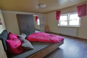 A bedroom with a bed, pillows, a wardrobe, a window with curtains, and a radiator. - Melitta holiday apartment (Heiligenberg)