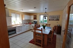 A kitchen with white cabinets, a dining table with chairs, and a hanging light fixture. - Melitta holiday apartment (Heiligenberg)
