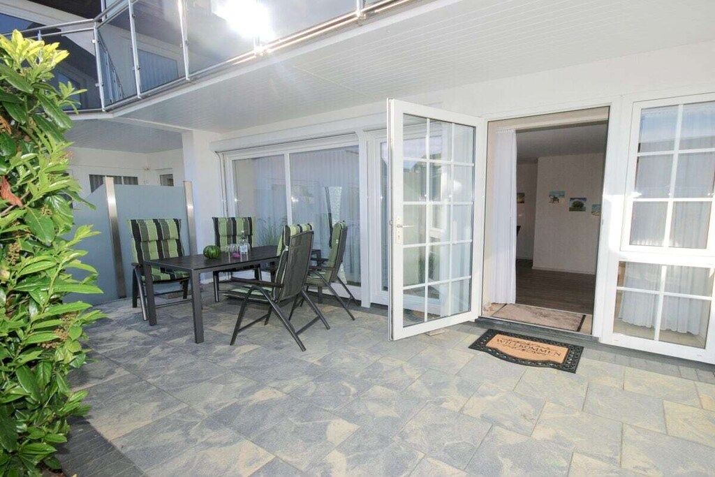 An outdoor dining area with a table and chairs, a glass door entrance, and a potted plant.