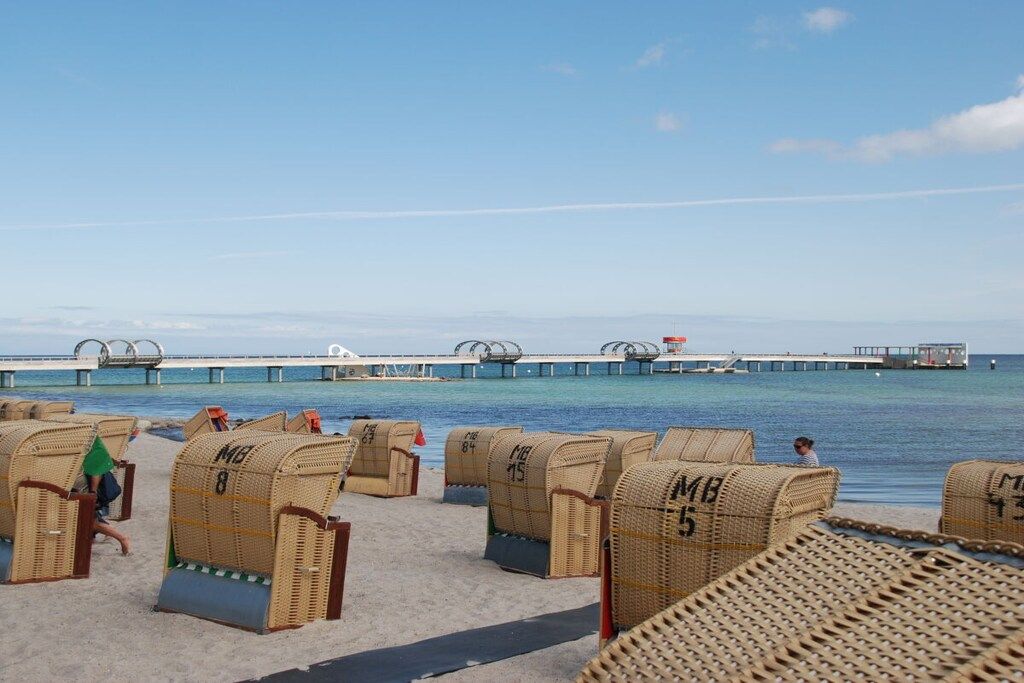 Beach chairs with numbers, a pier extending into the water, and a clear sky.