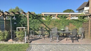 Une terrasse extérieure avec une pergola, une table et des chaises, ainsi qu’un chemin en briques.