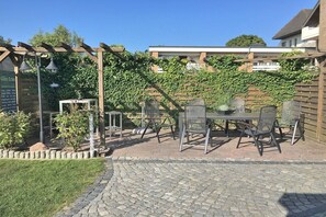 Een terras buiten, met een pergola, een tafel met stoelen en een pad van bakstenen.