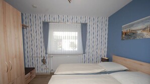 Une chambre avec deux lits, une armoire en bois, un radiateur et une fenêtre avec des rideaux.