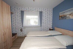 Een slaapkamer met twee bedden, een houten garderobe, een radiator en een raam met gordijnen.