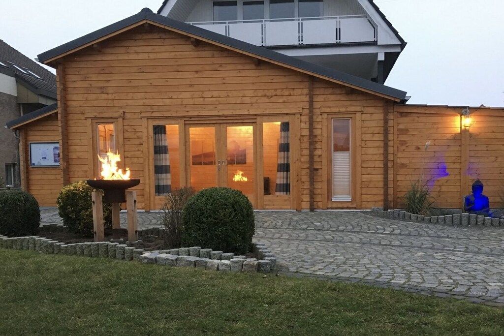 Un bâtiment en bois avec un foyer à l’entrée, une cour pavée de pierres et une statue en arrière-plan.