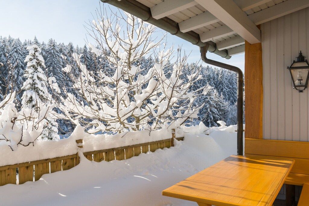 A wooden bench outside a building with a view of snow-covered trees.