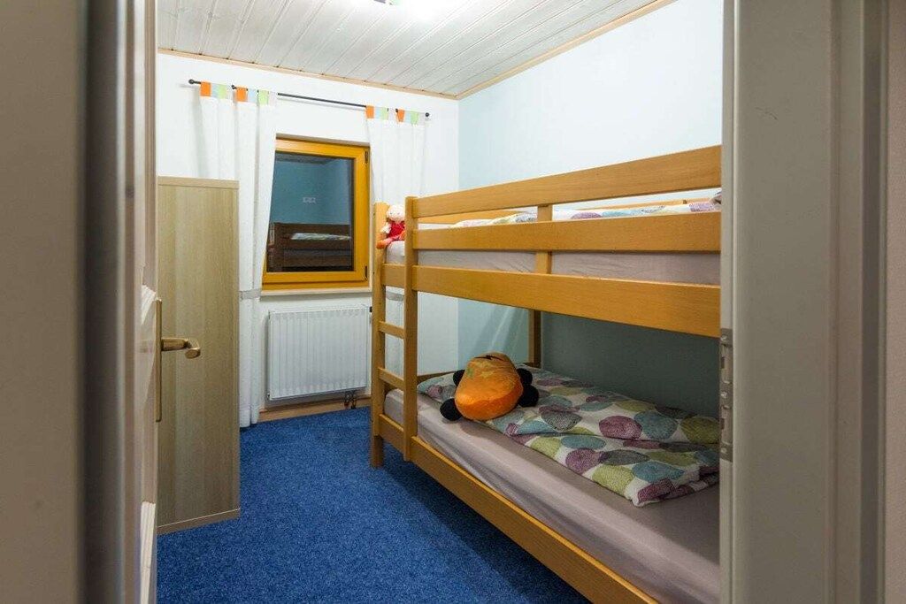 Een slaapkamer met stapelbed, raam, radiator en deur.