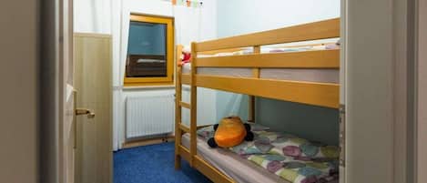 Une chambre avec un lit superposé, une fenêtre, un radiateur et une porte.