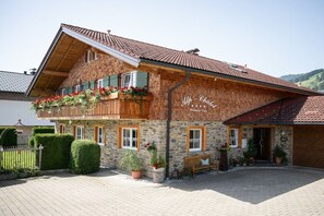 Edificio de dos plantas con fachada de piedra, balcones de madera con flores rojas y un letrero que dice 'Alp-Chalet Poltinshaus'.