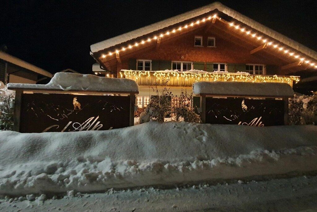 Un bâtiment recouvert de neige, illuminé par une lumière chaleureuse, et deux autres structures enneigées au premier plan.