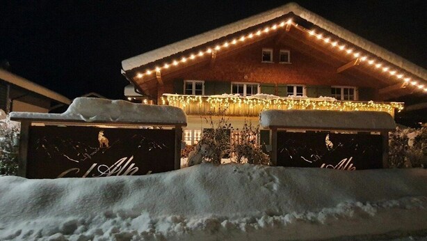 A snow-covered building with a warm light display and two snow-covered structures in the foreground. - Holiday apartment with 1 bedroom (Bolsterlang)