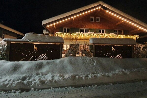 Un edificio cubierto de nieve con una exhibición de luces cálidas y dos estructuras nevadas al frente.