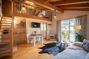 Een ruime woonruimte in loftstijl met een houten trap, een eettafel en een groot raam met gordijnen.