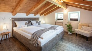 A bedroom with a large bed, wooden ceiling beams, a bedside table with a lamp, a potted plant, and a patterned armchair. - Holiday apartment with 1 bedroom (Bolsterlang)
