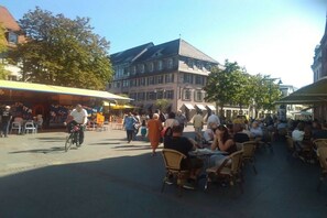 Ein Straßencafé mit Tischen und Stühlen, ein Radfahrer und Fußgänger auf einem Stadtplatz in Europa.