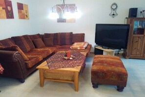 Ein Wohnzimmer mit Sofa, Hocker, Couchtisch, Fernseher und Schrank.