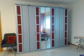 Ein Zimmer mit Schiebetürenschrank, einem Einzelbett, einem Sessel und einem kleinen runden Tisch.