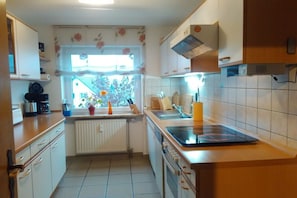 A compact kitchen with white cabinets, a built-in oven, a window with floral curtains, and a radiator. - Holiday apartment with 3 bedrooms (Wehr-Öflingen)